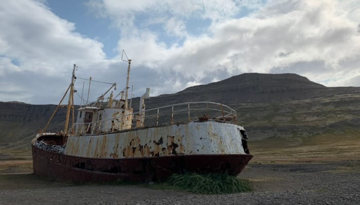 A steel ship rusting away on a beach, with a mountain rising up behind it.