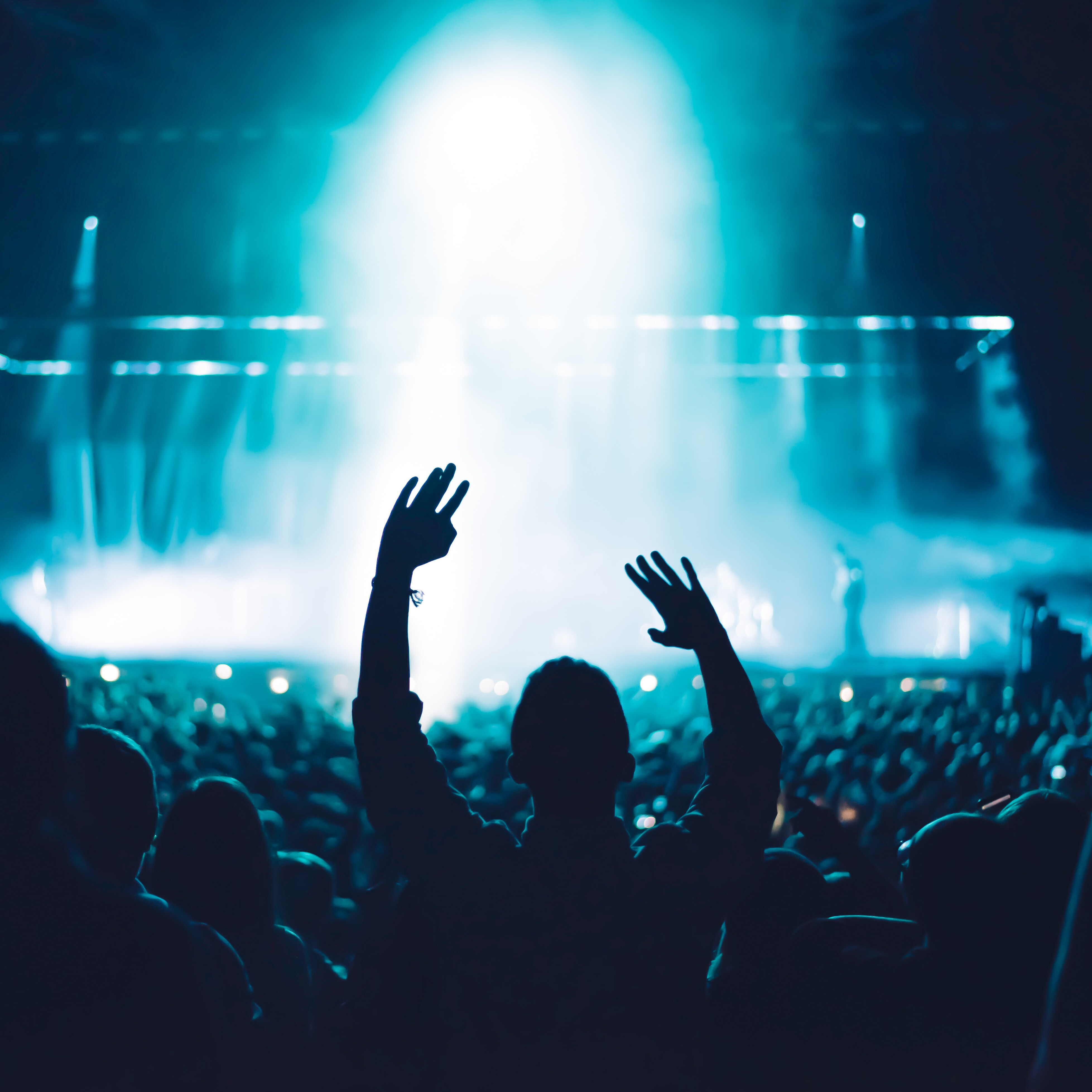 Blue smoky stage and crowd with person raising arms.