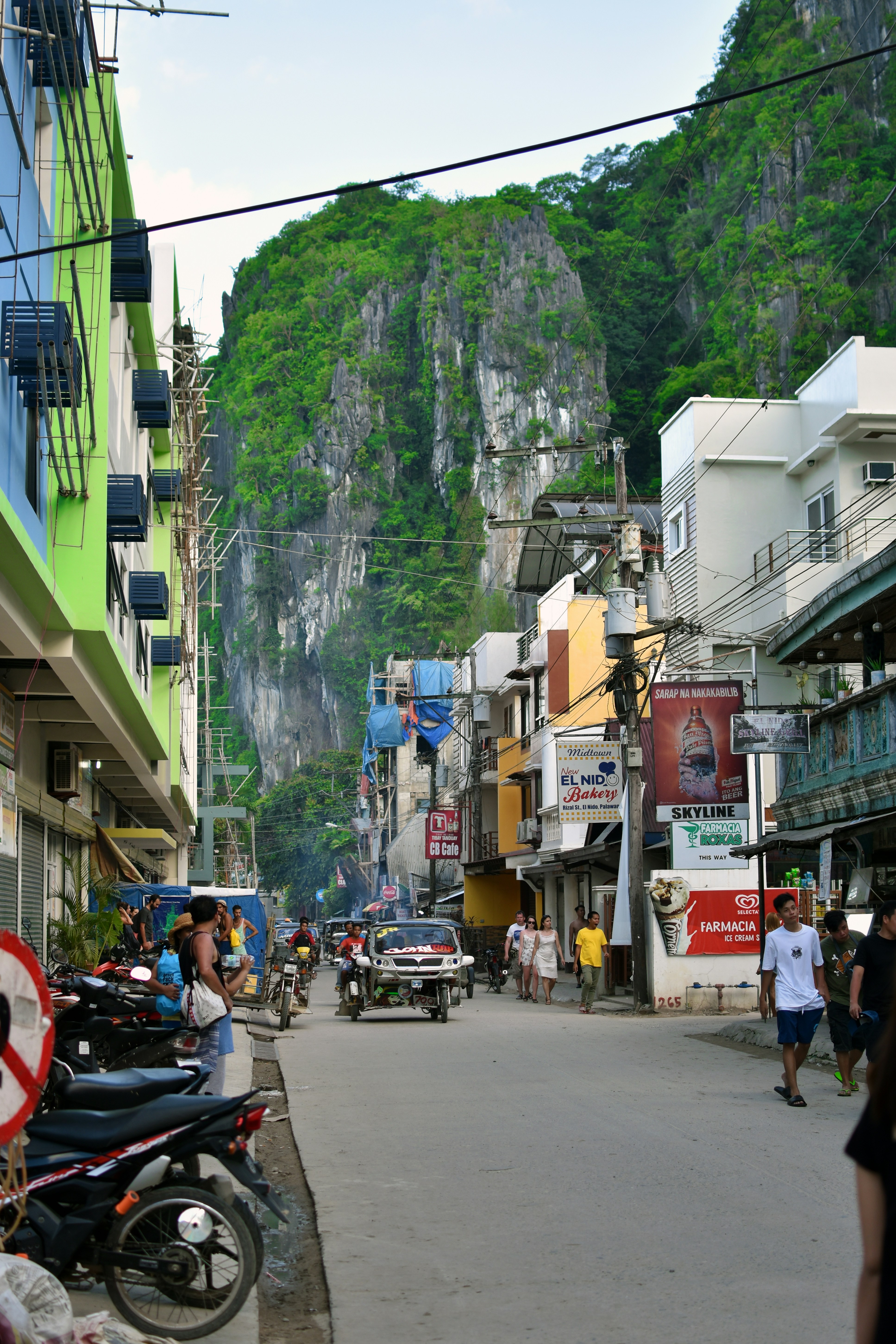 a street in the philippines lines with buildings and cars, with tall cliffs in the background