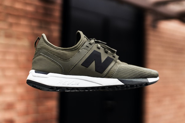 a New Balance sneaker in olive drab with a black logo