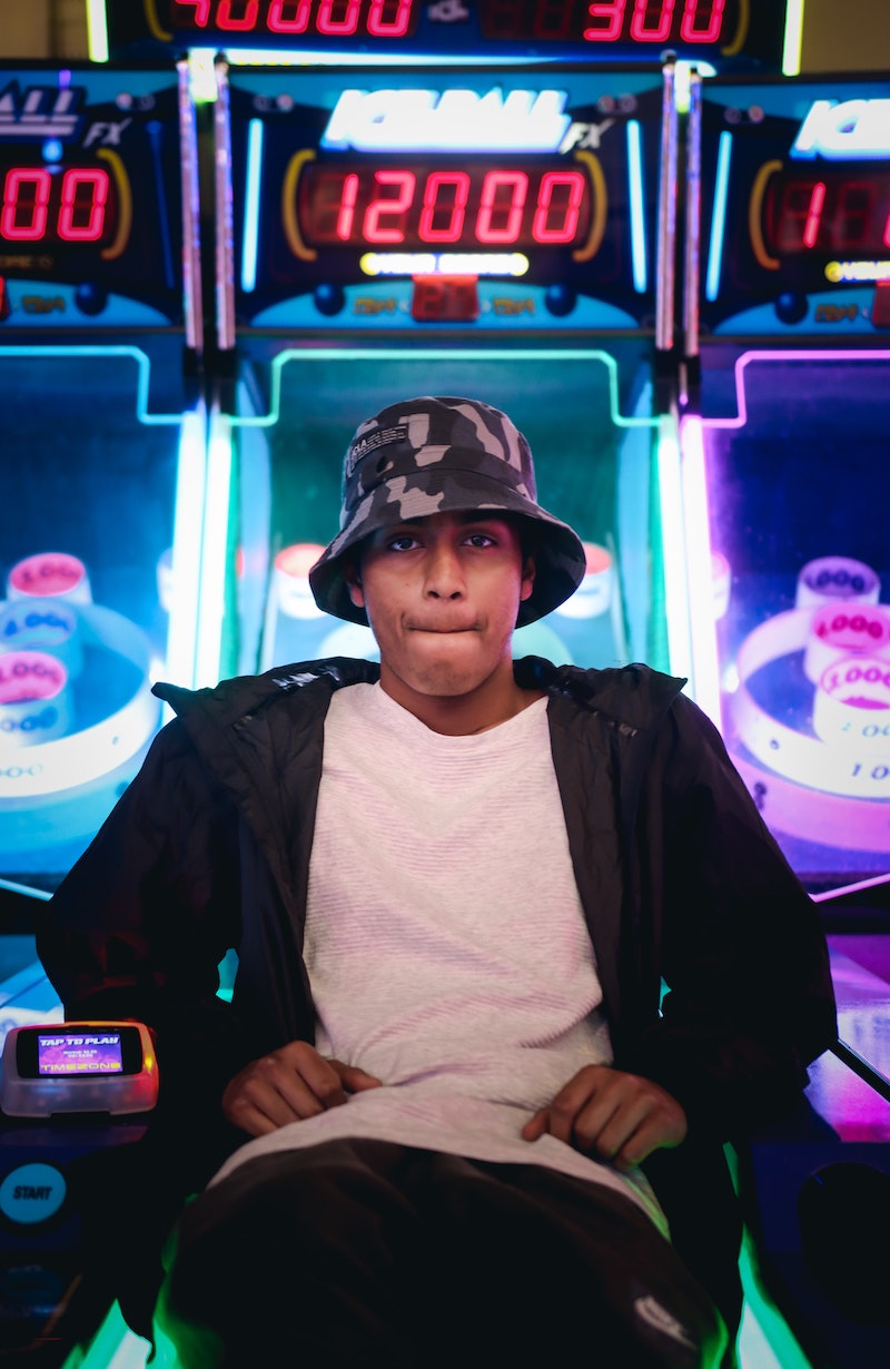 a person wearing a bucket hat, sitting on a skee ball machine lane. 