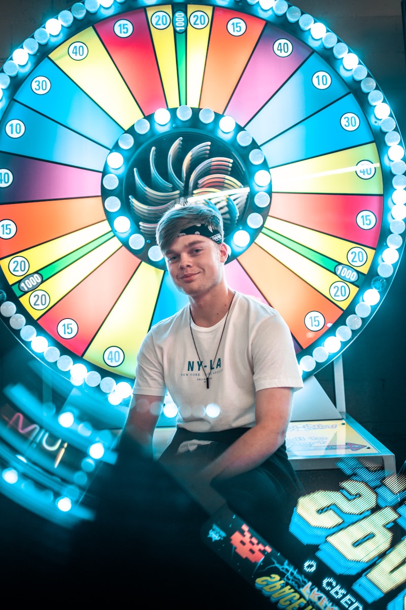 a person in a white t-shirt sitting on a wheel of fortune arcade game. 